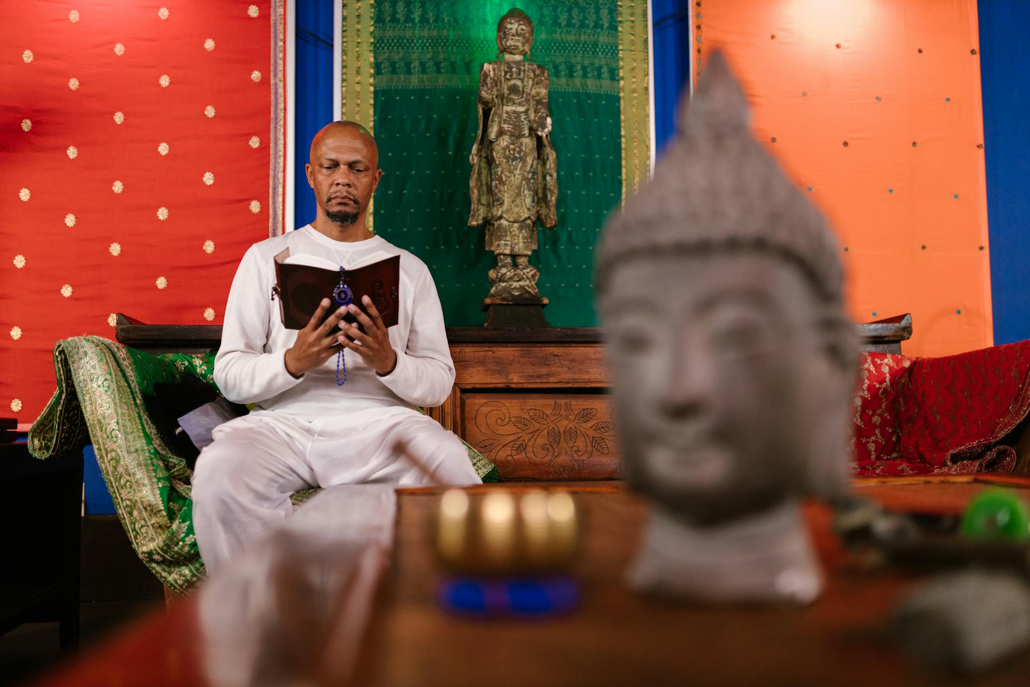 A man meditates indoors by a Buddha statue, embodying peace and spirituality.