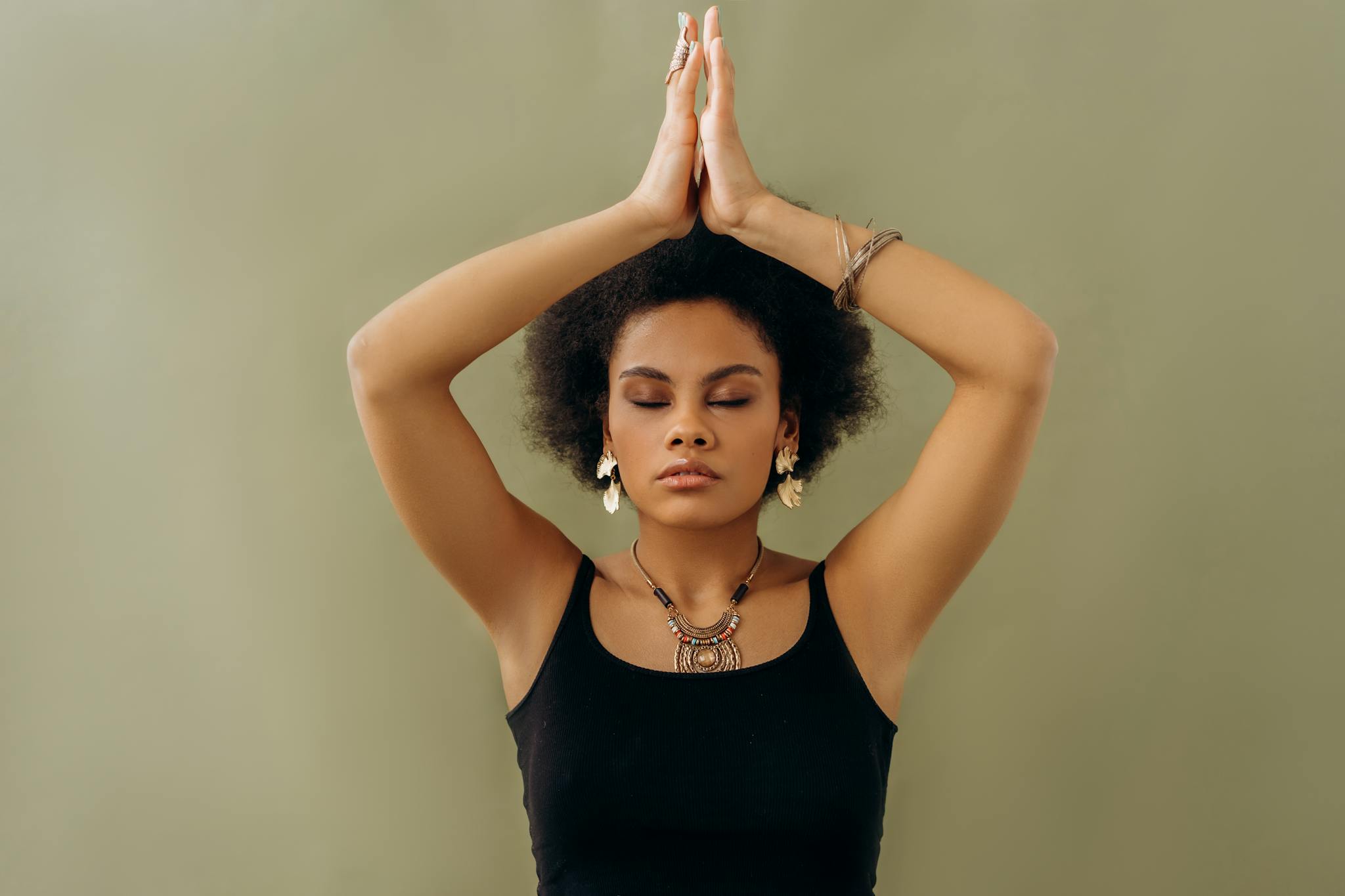 A woman in a black top meditates with closed eyes and hands in prayer pose, radiating calmness.
