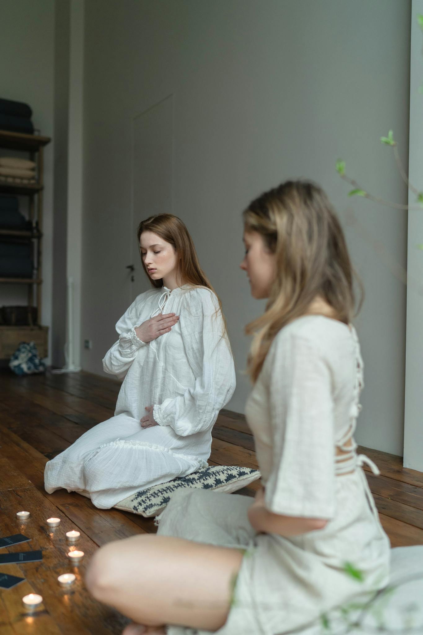 Two women meditating in a calm indoor setting surrounded by candles.